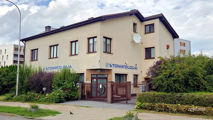 Widok z zewnątrz na gabinet dentystyczny Dental-Wit od strony ulicy. Widoczne wejście dla pacjentów, ogrodzenie oraz zieleń wokół budynku.